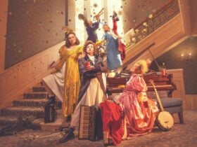 Four women in colorful, ornate Regency-era costumes pose dramatically on a staircase