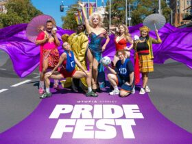 Pride Fest performers stand on purple road in various poses. The words Pride Fest are at their feet