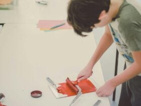A teenage practises printmaking with a roller and red paint