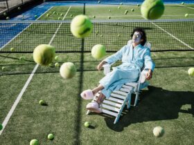 A man relaxing on a chair in a tennis court, wearing a robe, slippers and a face mask.