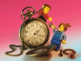 Two LEGO minifigures interact with an open, worn pocket watch, against a pinkâtoâblue background