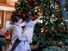 Mother holding her child who is standing near a christmas tree