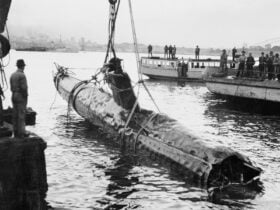 Several men watch as a Japanese midget two-man submarine is raised from the harbour bed.