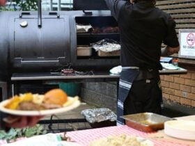 Meat smoking in smoker with table of salads in foreground