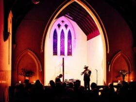 A brightly illuninated church sanctuary with the silhouettes of a pianist, violinist and audience
