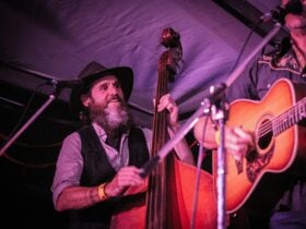 A bearded man plays double bass, to the edge of the photo is a guitar being played by an unseen fig