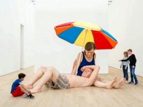 A surreal art installation featuring giant, realistic sculptures of couple under a colorful umbrella