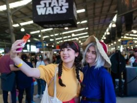 Two friends taking a selfie in cosplay at a crowded convention with a Star Wars sign above.