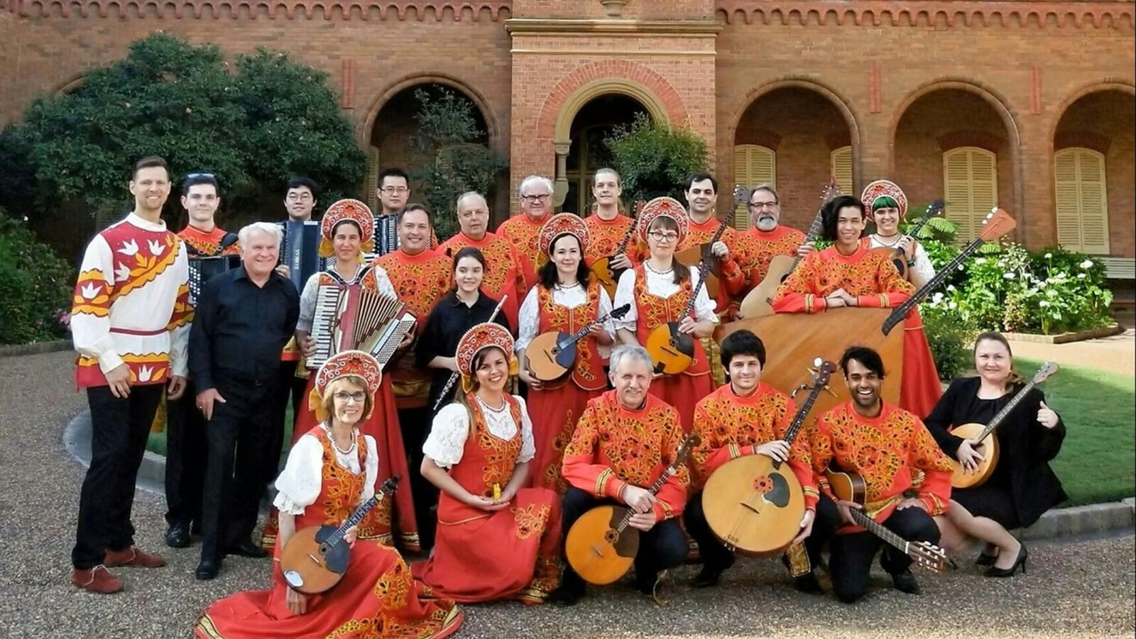 Members of the orchestra posing together in front of a building, some holding instruments