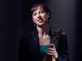 Madeleine Easton suits against a black background with a violin
