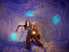 A man and woman explore a cave surrounded by glowing blue lights