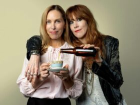 Two women, one dressed in black leather holding a beer and the other dressed in pink with a coffee
