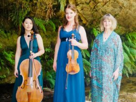 Three artists stand together with a backdrop of lush trees