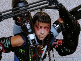 Person in detailed sci-fi costume with mechanical arms, futuristic makeup, and intense expression,
