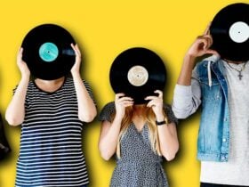 A group of people in a line, holding a vinyl record in front of their faces