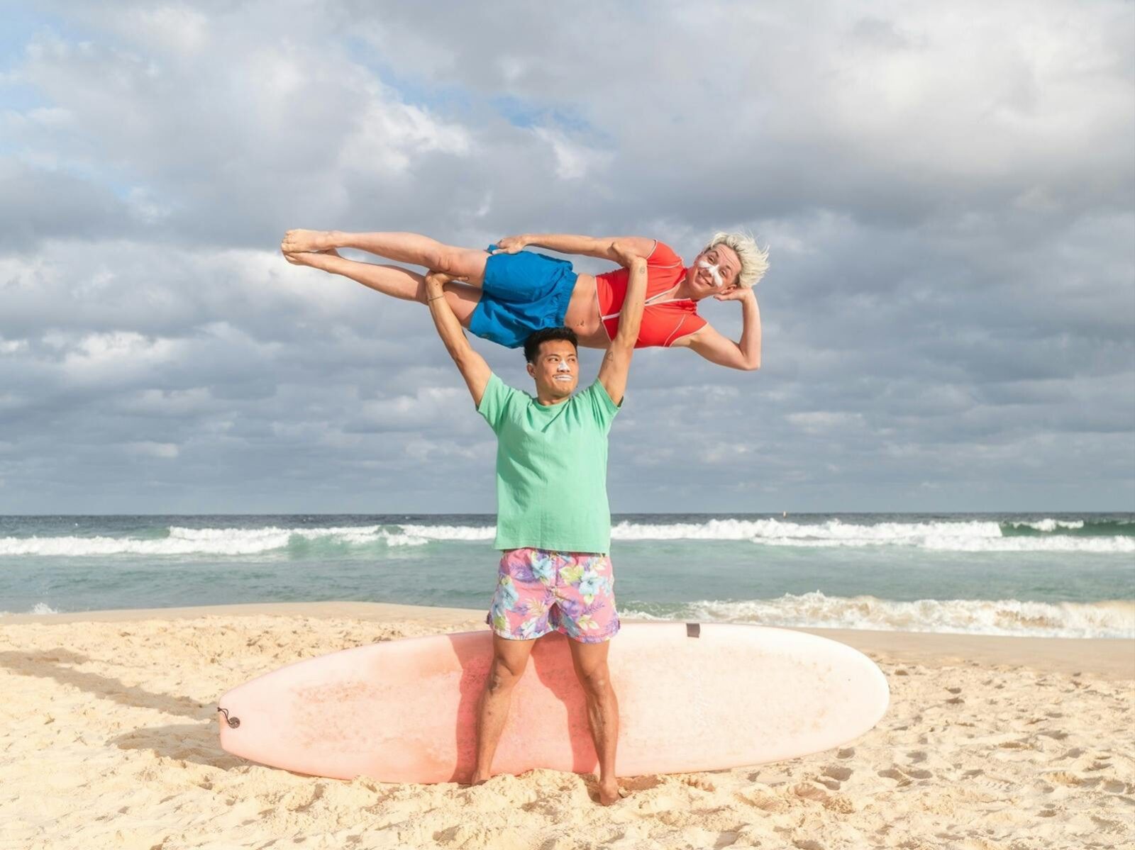 Two acrobats, dressed as surfers on a beach