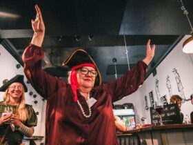 An older woman in a red shirt and a pirate hat dances for joy