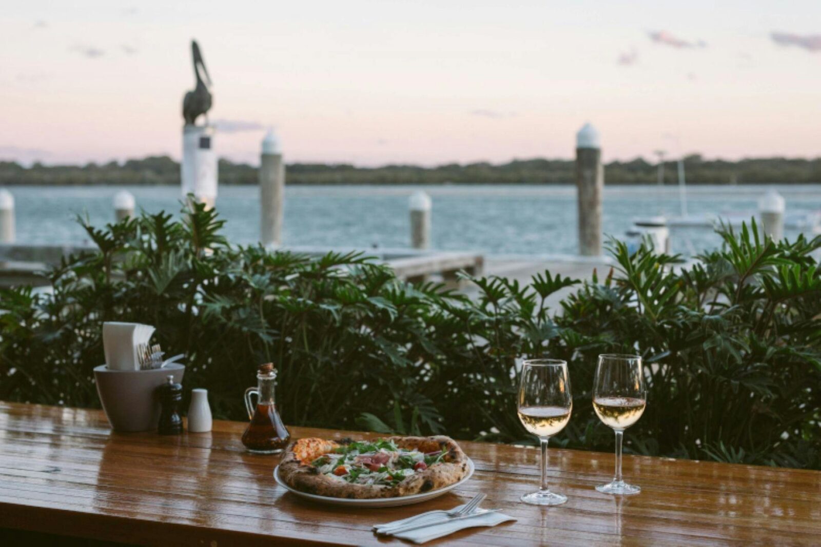 pizza and wine on timber table with river and wharf in background
