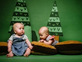 Two babies sitting and playing in front of a paper forest background