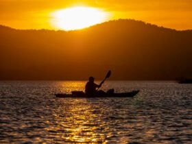 Silhouette of a kayaker at sunset with golden light and mountains in the background.