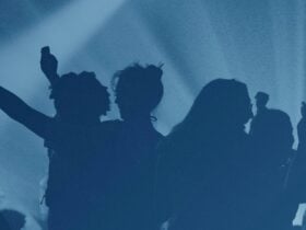 Silhouettes of people holding their hands up at a concert, lit by blue stage lighting.