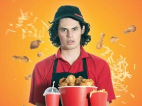 A young man in a fast-food uniform looks bewildered as fried chicken and chips fly around him.