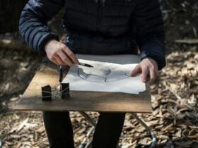 Workshop participant sits on a stool outside holding a boardthat he is making a drawing on top of