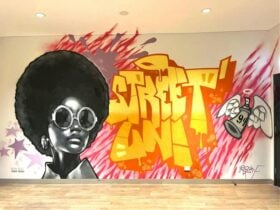 Mural artwork with a woman wearing sunglasses and pink and yellow lines in background.