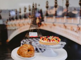 Table setting with a crossaint, a fruit flan and a statue of the Eiffel Tower in the background.