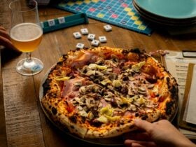 Hand reaching for pizza with a beer, menu and scrabble game pieces