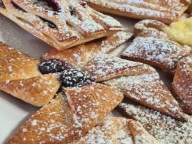 Various Danishes covered in icing sugar, some with berries and some with chocolate.