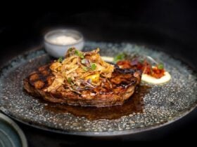 A piece of steak on a place with garnish and sauce on the side