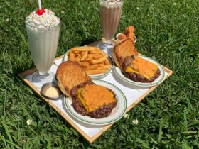 2 burgers, 2 milkshakes and a serve of fries sitting on a tray, on the grass