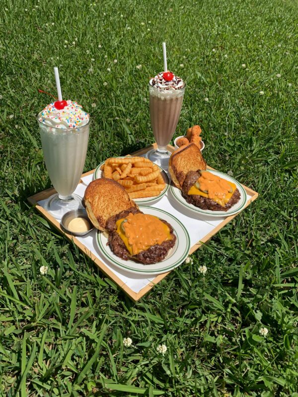 2 burgers, 2 milkshakes and a serve of fries sitting on a tray, on the grass