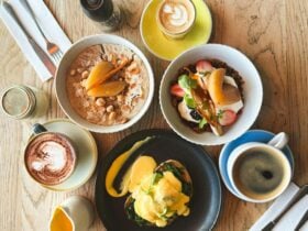 Top view of various breakfast items including coffee, eggs benedict, granola bowl & pear porridge.