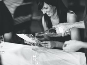 A young woman smiles broadly while reading a brochure and having cider poured for her in a cellar