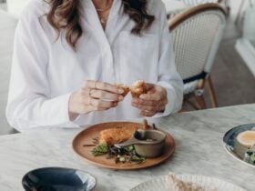 A close up of a woman sitting at a table, breaking the crab stick in half over her plate