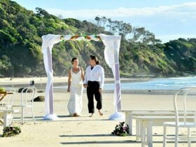 A couple under a wedding arch on Wategos Beach in Cape Byron State Conservation Area. Photo: Fiora