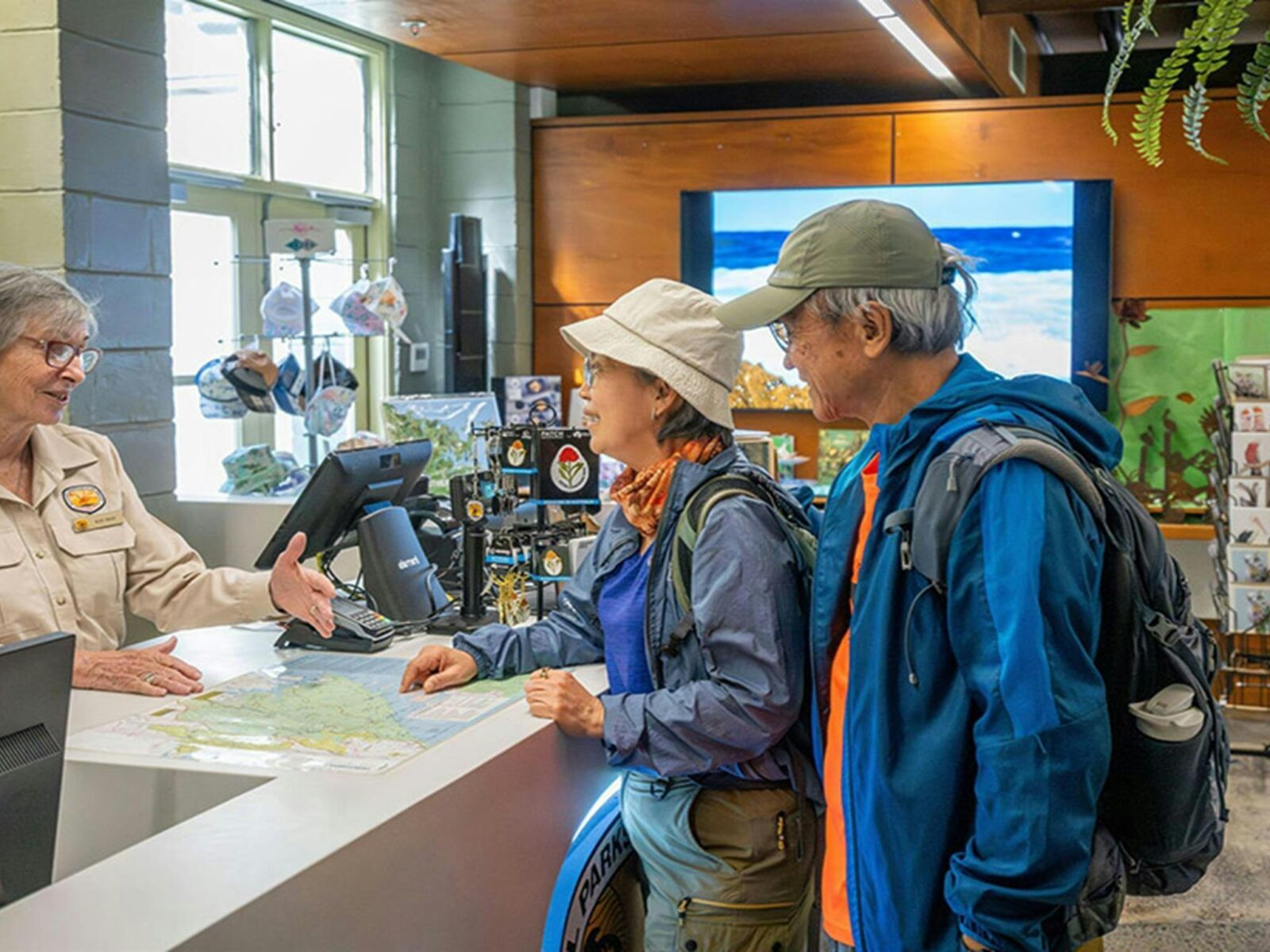 An NPWS staff member assisting 2 visitors inside the Royal National Park visitor centre at The Royal