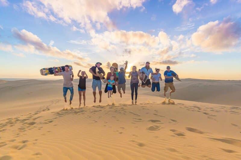 A group of all ages jumping in the air at the top of a sand dune