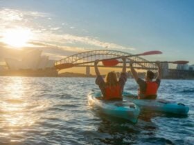 Double kayak sunrise tour in Sydney with paddlers raising oars above the Opera House.