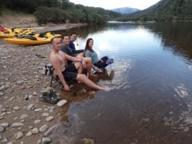 A group of people are sitting in the snowy river on chairs soaking there feet