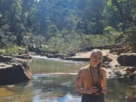 A woman stands in front of a gentle creek and lush bushland