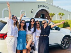A small group of six smiling tourists standing in front of a modern white luxury transport vehicle o