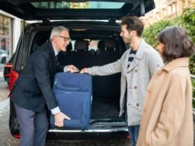 Taxi driver assisiting passengers with bags in the back of a car