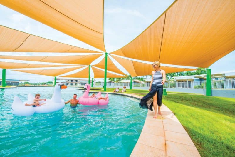 humongous blue pool covered by shade-cloth. A mother walks along the edge, while dad and kids swim