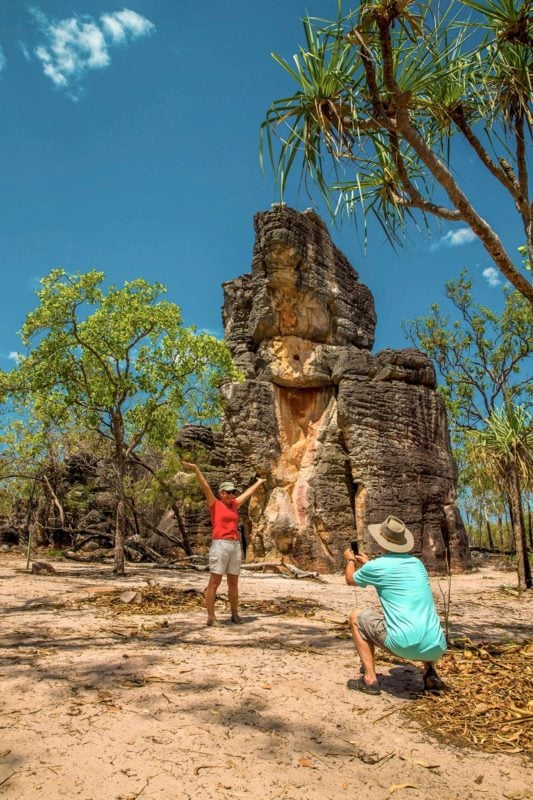 Woman standing infront of a large rock formation while husband takes photo