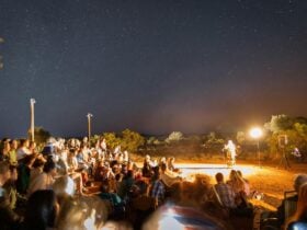 Group of people in the audience (faces obscured) watching poet Victoria Alondra perform in the dark