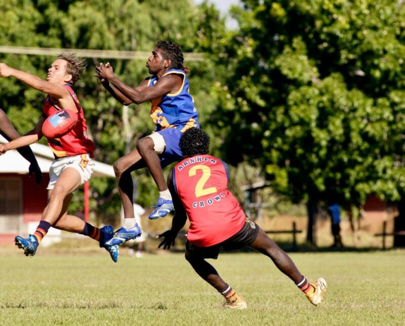 Three sports players vying for a red AFL ball