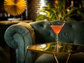 A velvet green couch as the backdrop of a cocktail on a glass table inside the cocktail lounge